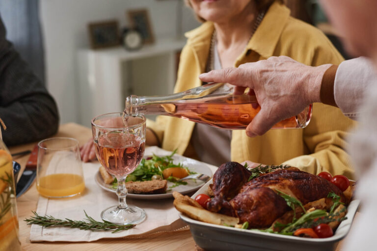 Close-up of man pouring wine in glass from the bottle while having dinner with his friends